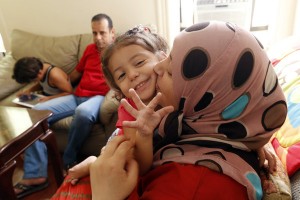 In this Wednesday, Sept. 16, 2015 photo, Maaesa Alroustom, center, is kissed by her mother, Suha, as her father, Hussam, back, sits with her brother Wesam in their apartment in Jersey City, N.J. The Alroustoms are Syrian refugees after fleeing their war stricken country. (AP Photo/Julio Cortez)