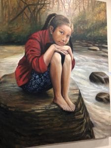 girl sits on a large rock in the middle of a stream with her knees pulled up and her chin resting on her knees.